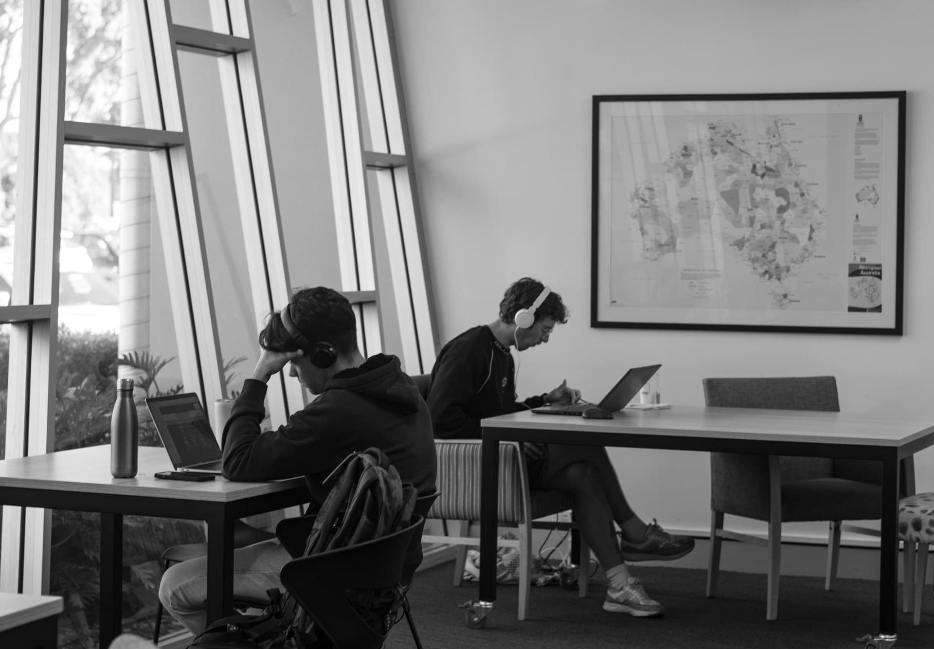 Two students working on laptops in a sunlit study space